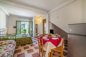 A dining area with a table set for two, a bed with floral bedding, and a modern refrigerator. - Family Village M7 Pool And Sea (Otranto)
