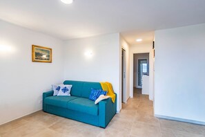 Un sofá azul turquesa con cojines estampados, un cuadro en la pared y un pasillo que conduce a otra habitación.
