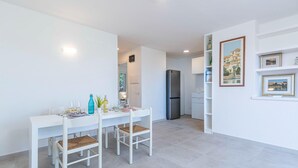 Eine moderne Küche mit weißen Schränken, einem Edelstahlkühlschrank und einem Essbereich mit weißem Tisch und Stühlen.