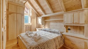 A wooden cabin bedroom with a bed, a nightstand, and built-in wooden cabinets. - Baita Delle Stelle in Scarlino (Sauze di Cesana)