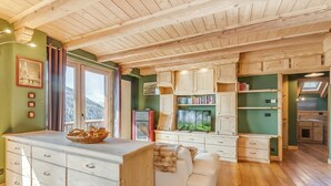 A cozy, well-lit room with wooden ceilings, a large window, a white sofa, and a wooden cabinet with books. - Baita Delle Stelle in Scarlino (Sauze di Cesana)