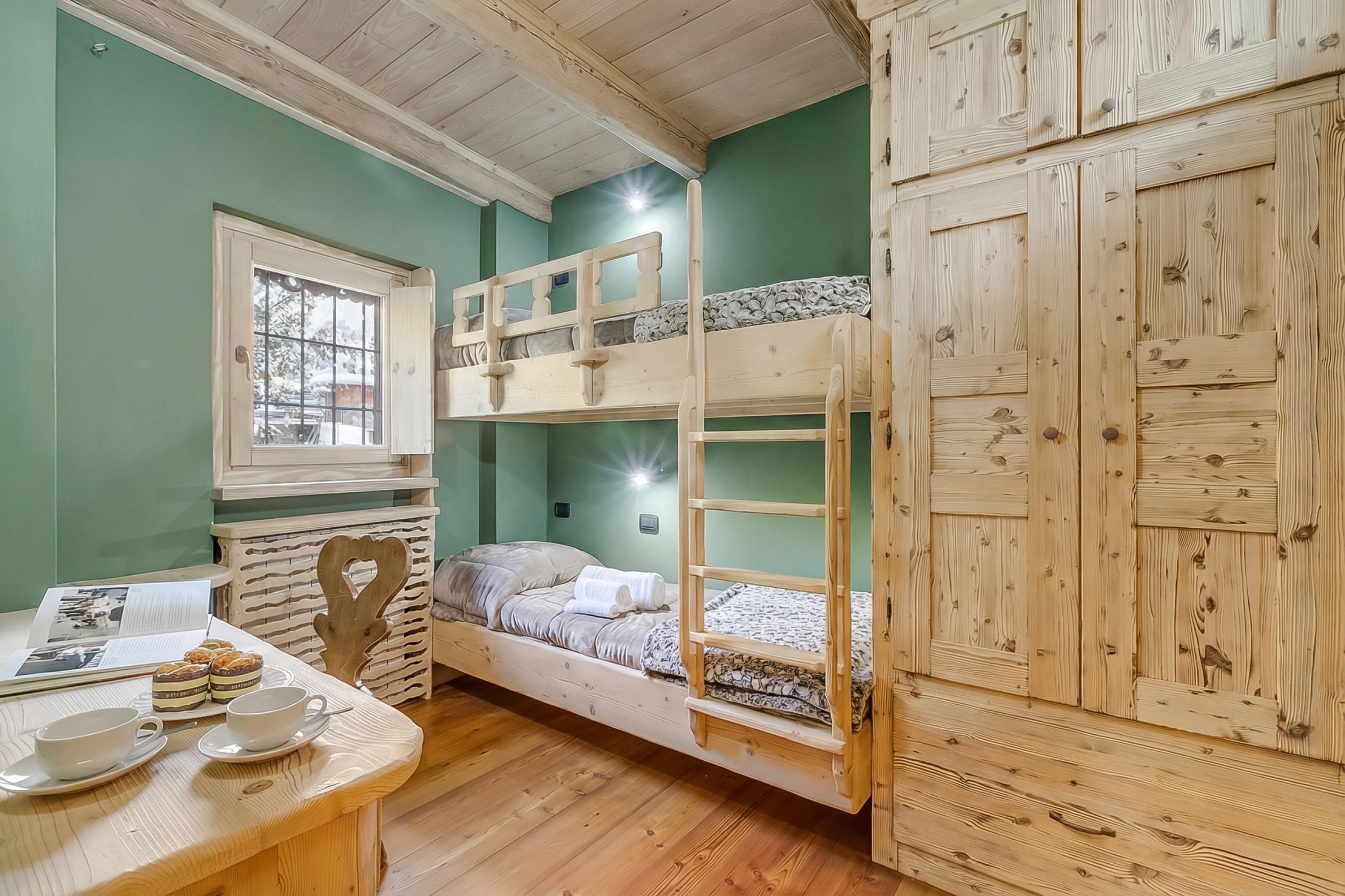 A bunk bed room with a wooden ladder, a desk with a heart-shaped chair, and a window.
