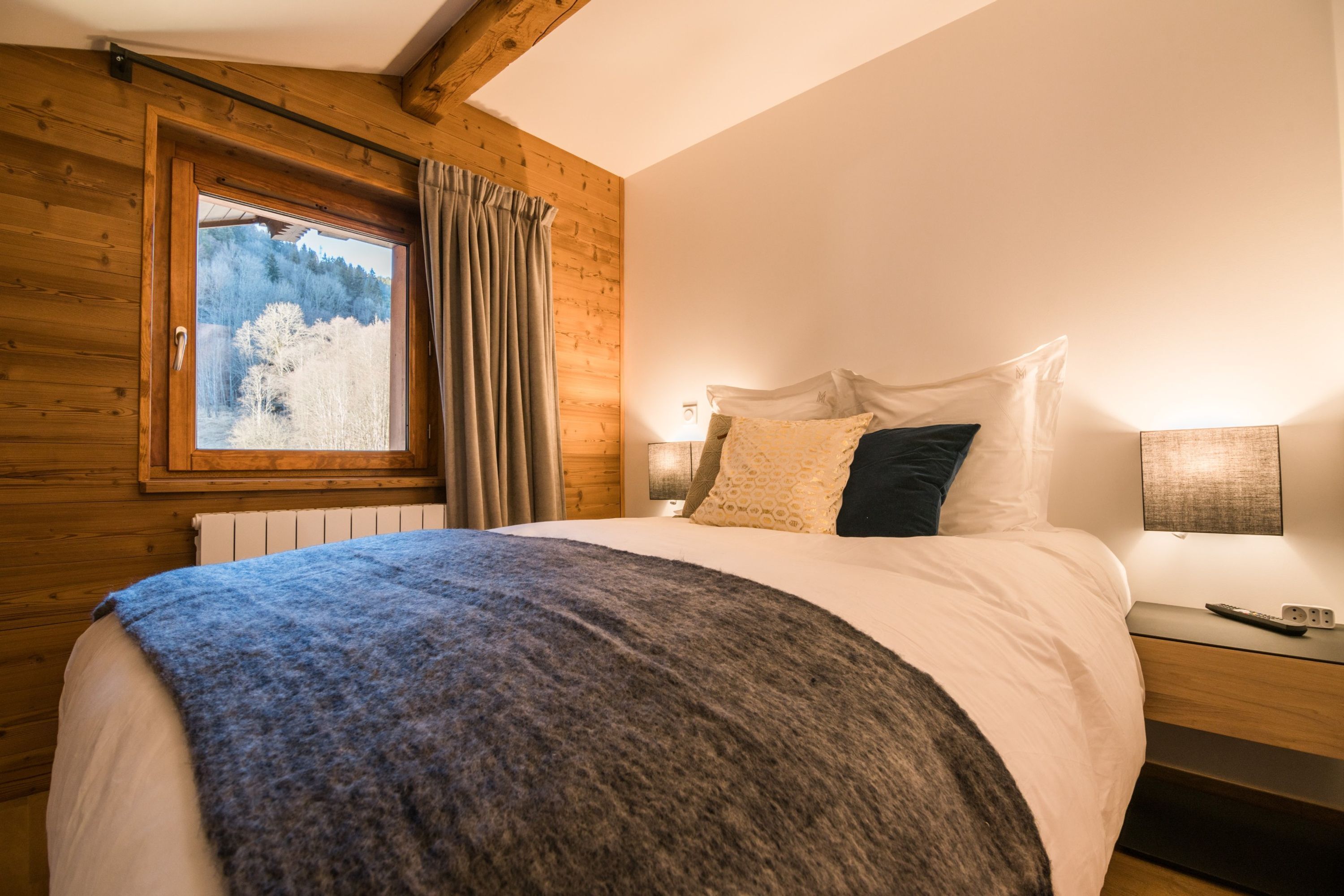 Ein Schlafzimmer mit einem großen Bett, Holzwänden, einem Fenster mit Vorhängen und einem Nachttisch mit Lampe.