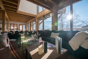 A spacious room with a high ceiling, wooden beams, large windows, a sofa, a coffee table, and a dining area. - R Sidence Les Portes de Meg ve C58e (Praz-sur-Arly)