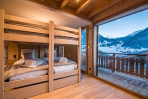 Una baita di legno con letti a castello, un balcone con ringhiera di legno e vista sulle montagne innevate.