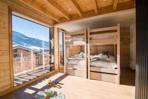 Una baita di legno con letti a castello, un'ampia finestra vista montagne innevate e un'uscita su un patio in legno.