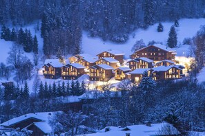 Un lodge imbiancato dalla neve con diverse cabine di legno, circondato da alberi e un paesaggio innevato.