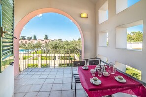 A balcony with a table set for tea, a view of a garden, and a building in the background. - Family Village M6 Pool And Sea (Otranto)