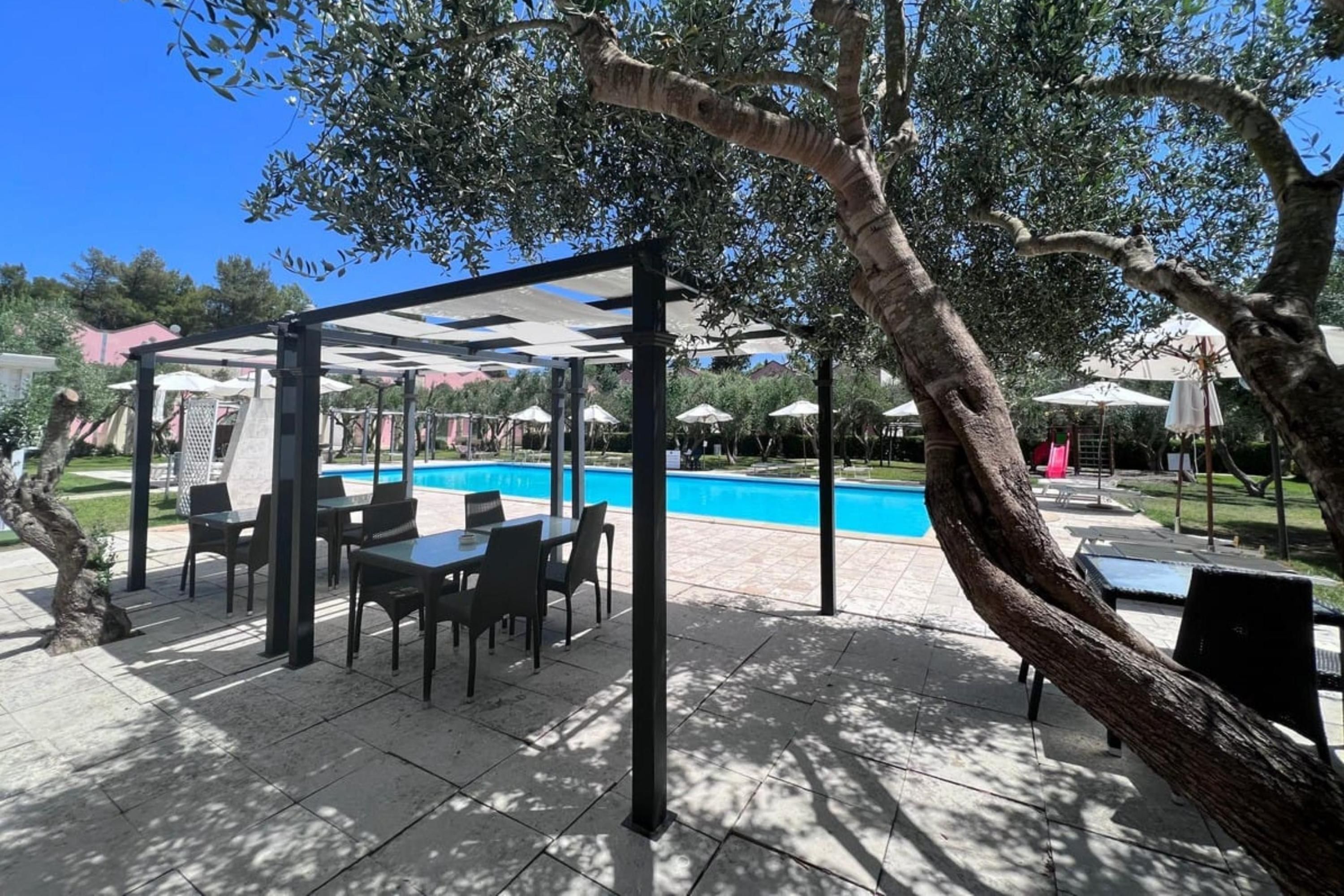 En uteplats med pool, ett takförsett sittområde och träd.