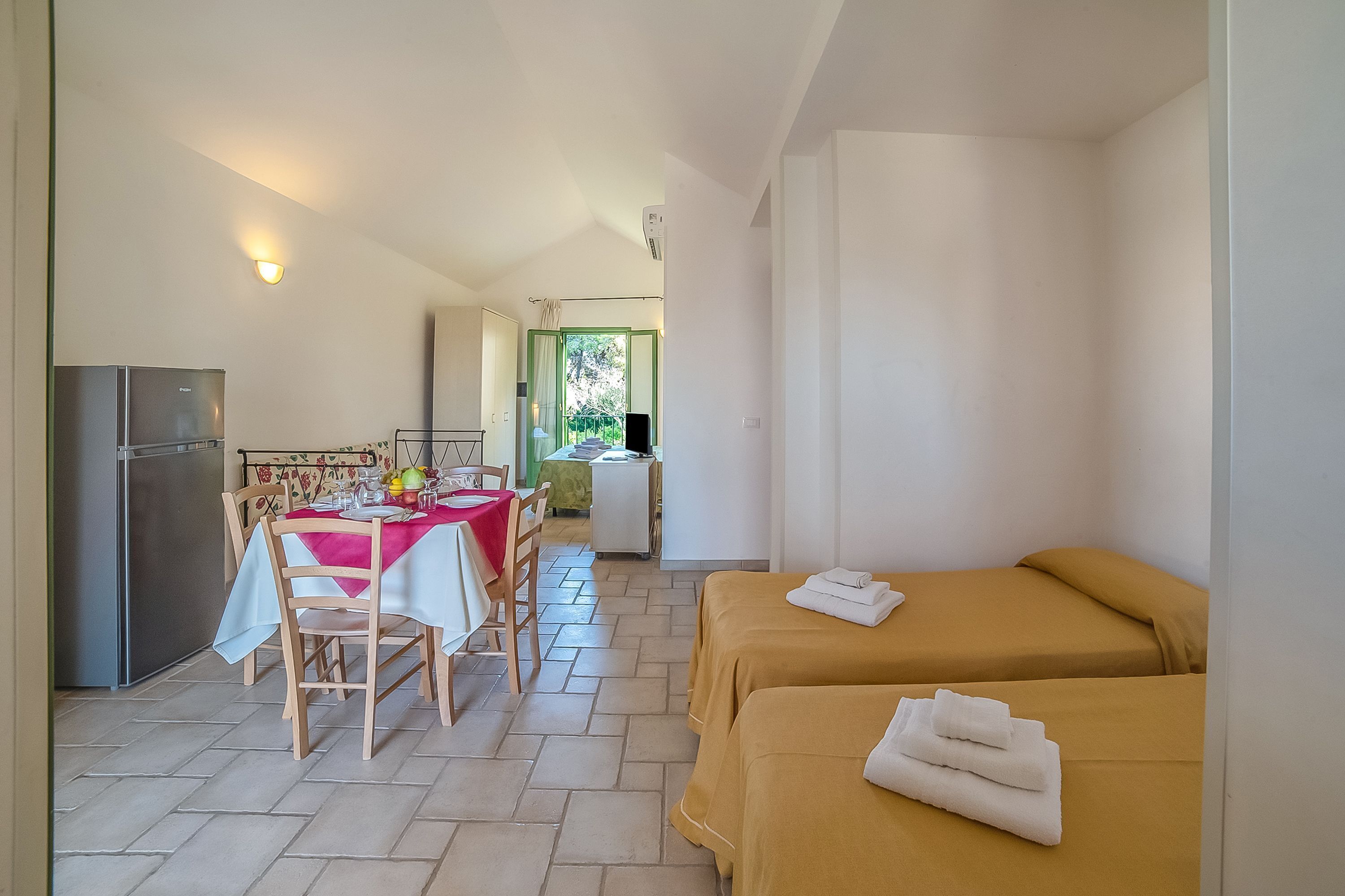 A room with two beds, a dining area with a table and chairs, and a refrigerator.