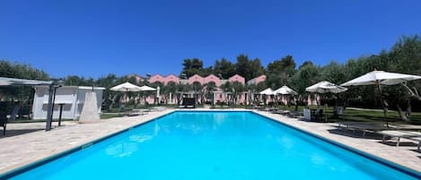 A rectangular swimming pool with a clear blue water surface, surrounded by lounge chairs and umbrellas.