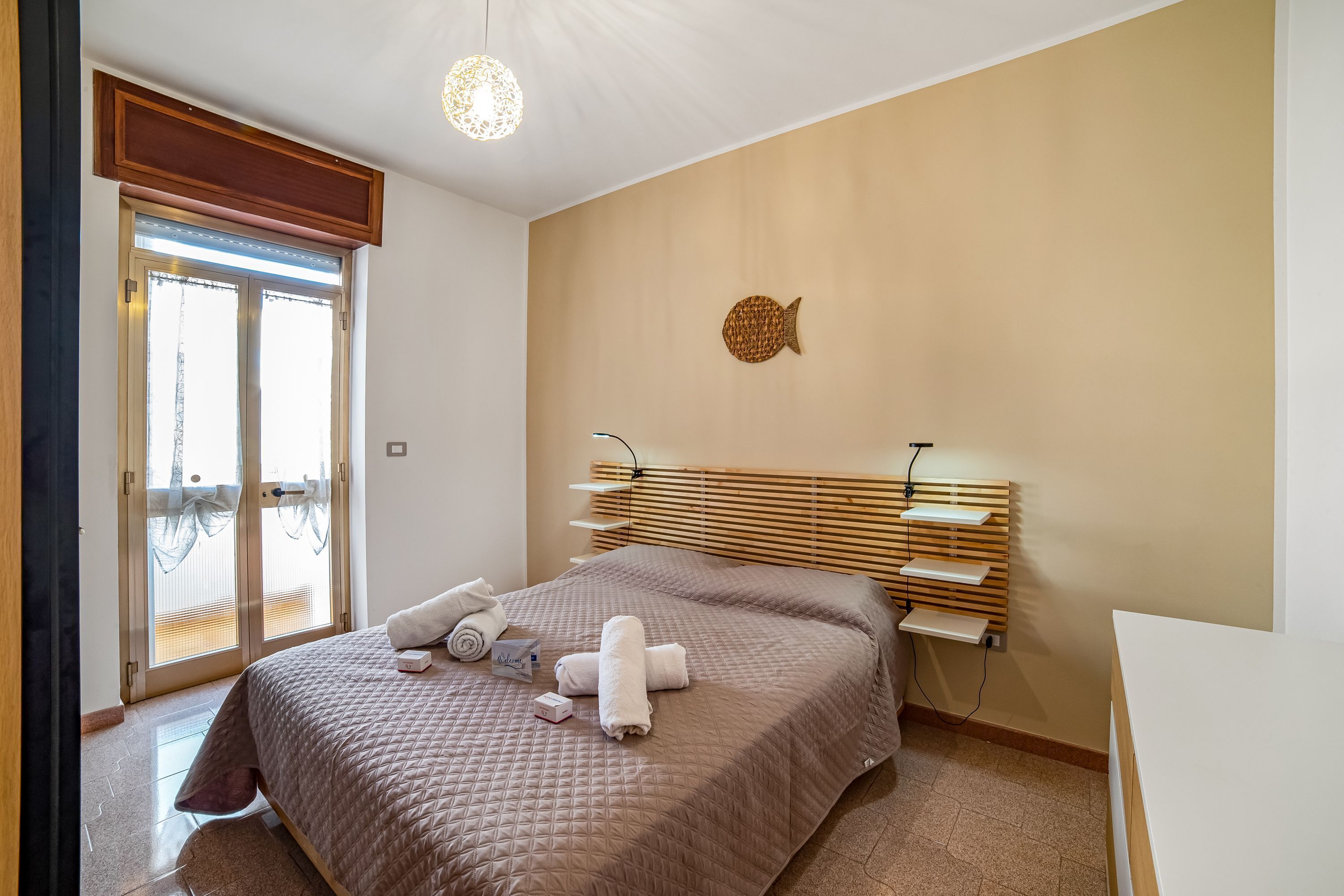 A bedroom with a bed, a headboard, a wall decoration, and a window with blinds.