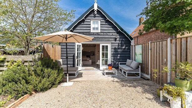 A wooden house with a sloped roof, a front porch with a bench and table, and a garden area with potted plants. - Holiday Home - Schoolstraat 6a Vrouwenpolder (Vrouwenpolder)