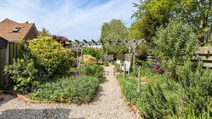 A garden pathway leading to a wooden pergola with a gravel path and various plants. - Holiday Home - Schoolstraat 6a Vrouwenpolder (Vrouwenpolder)
