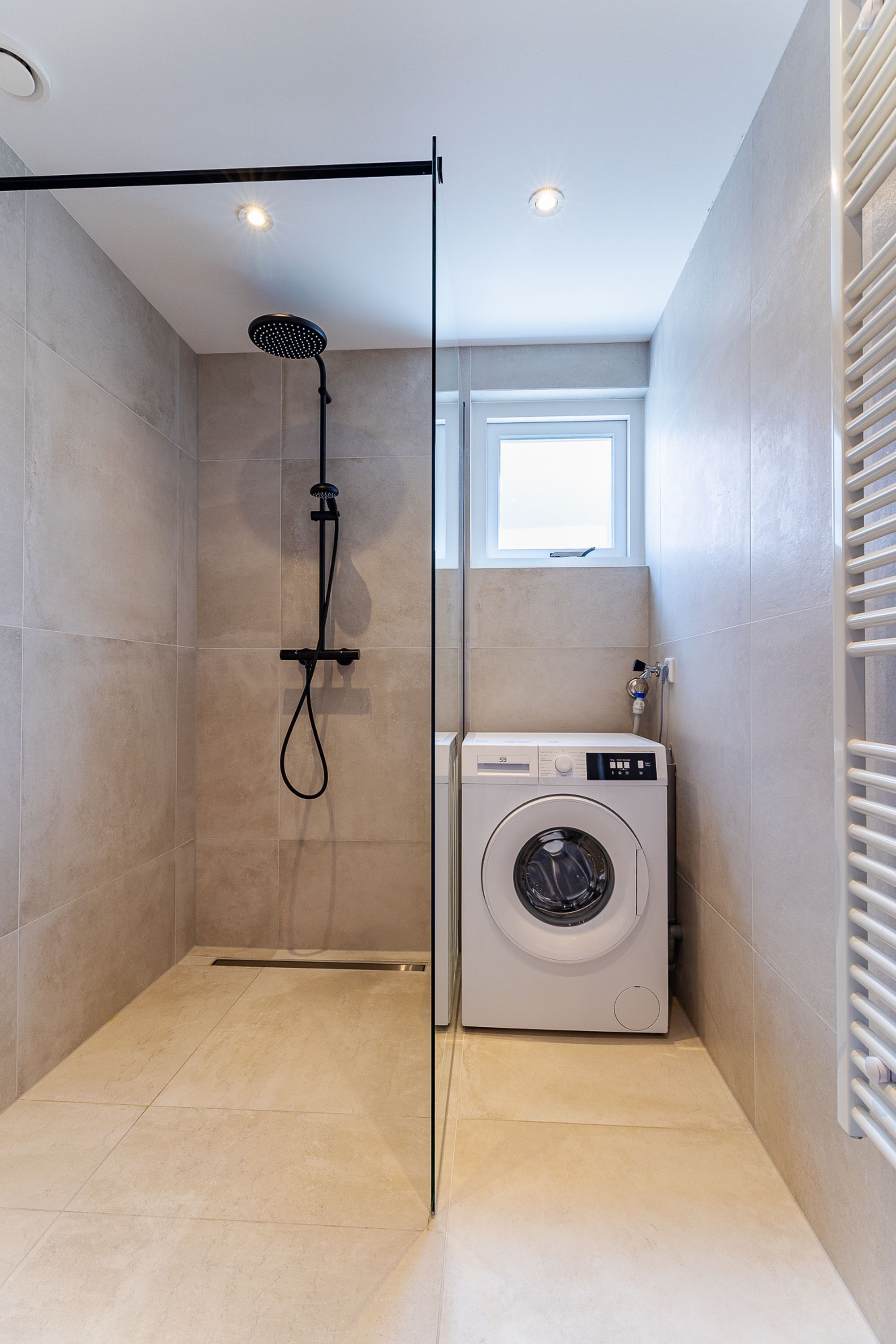 Un baño pequeño con ducha, lavadora integrada y ventana.