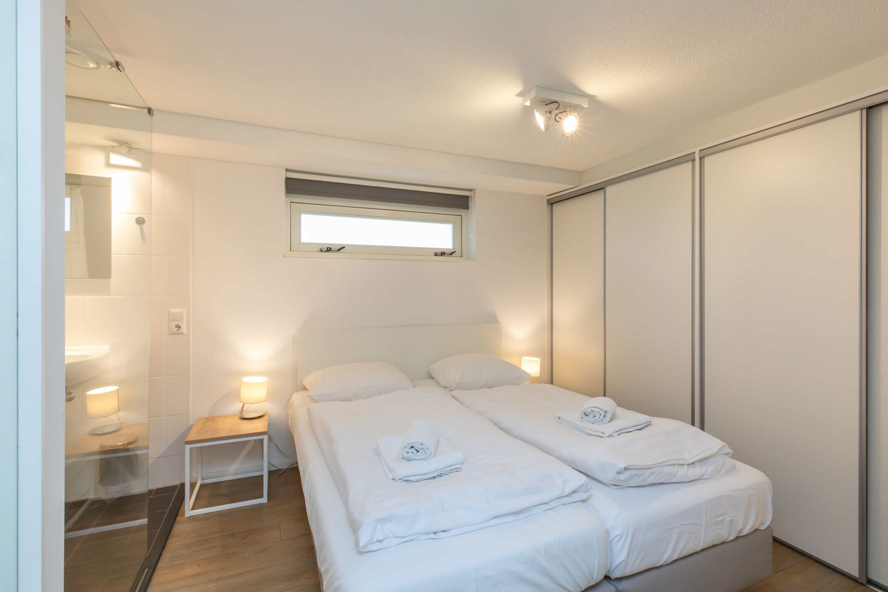 Een hotelkamer met twee bedden, een klein nachtkastje met lamp, een raam en een schuifdeurkast.