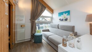 A cozy room with a sofa, a small ottoman, a radiator, a window with curtains, and a painting on the wall. - Zonnedorp 21 Beach Villa Joya Renesse Luxury Beach Villa With Sauna (Renesse)