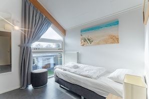 A bedroom with a bed, a window with curtains, a radiator, and a painting on the wall. - Zonnedorp 7 De Meerpaal in Renesse Comfortable Holiday House Close to the Beach (Renesse)