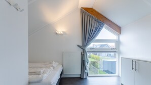Un dormitorio con cama, un radiador, una ventana con cortinas, una viga de madera y un armario blanco.