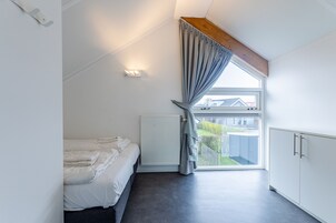 A bedroom with a bed, a radiator, a window with curtains, a wooden beam, and a white wardrobe.