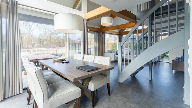 Un comedor moderno con una mesa y sillas de madera, una escalera y vistas al exterior.
