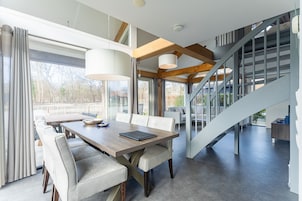 A modern dining area with a wooden table and chairs, a staircase, and a view of the outdoors.