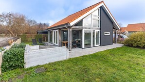 Una casa moderna con techo inclinado, grandes ventanales y un patio.