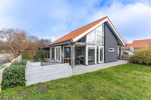 A modern house with a sloped roof, large glass windows, and a patio area.