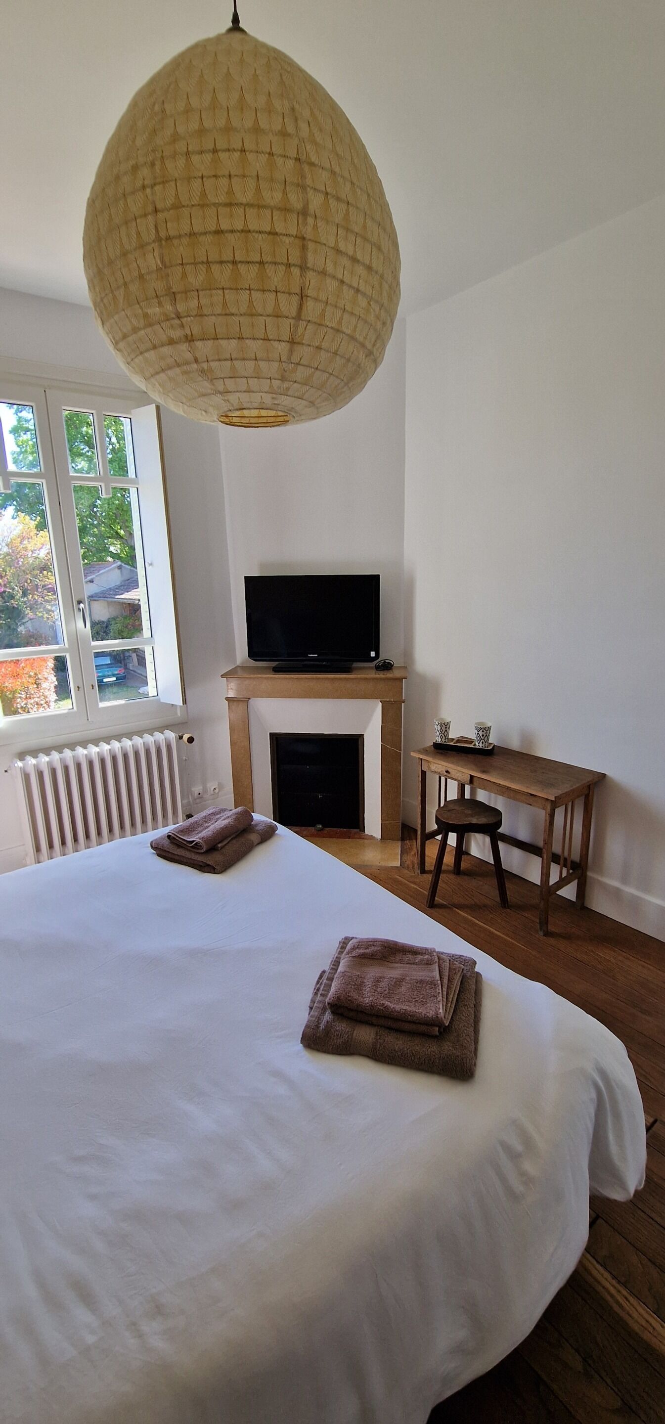 Une chambre avec un grand lit, un téléviseur posé sur un meuble, un bureau en bois et un luminaire suspendu.