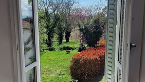 A room with a window overlooking a garden, a radiator below the window, and a wooden floor. - Chambre 2 Duc de Bouillon (Maringues)