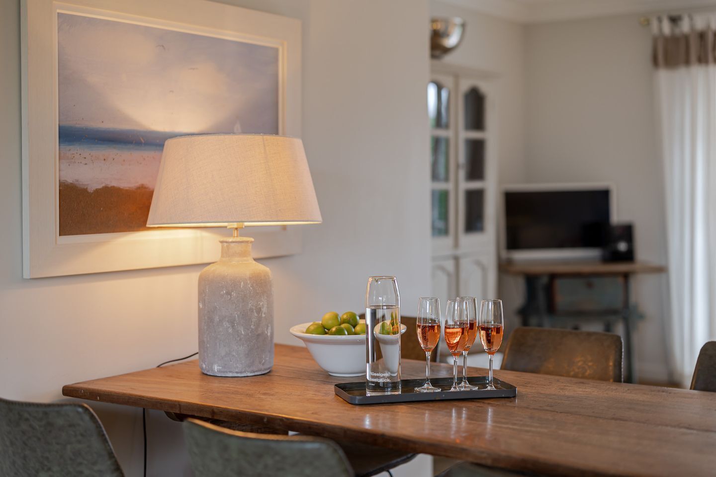 Une table à manger avec une lampe, un bol d’olives et quatre verres de vin rosé.