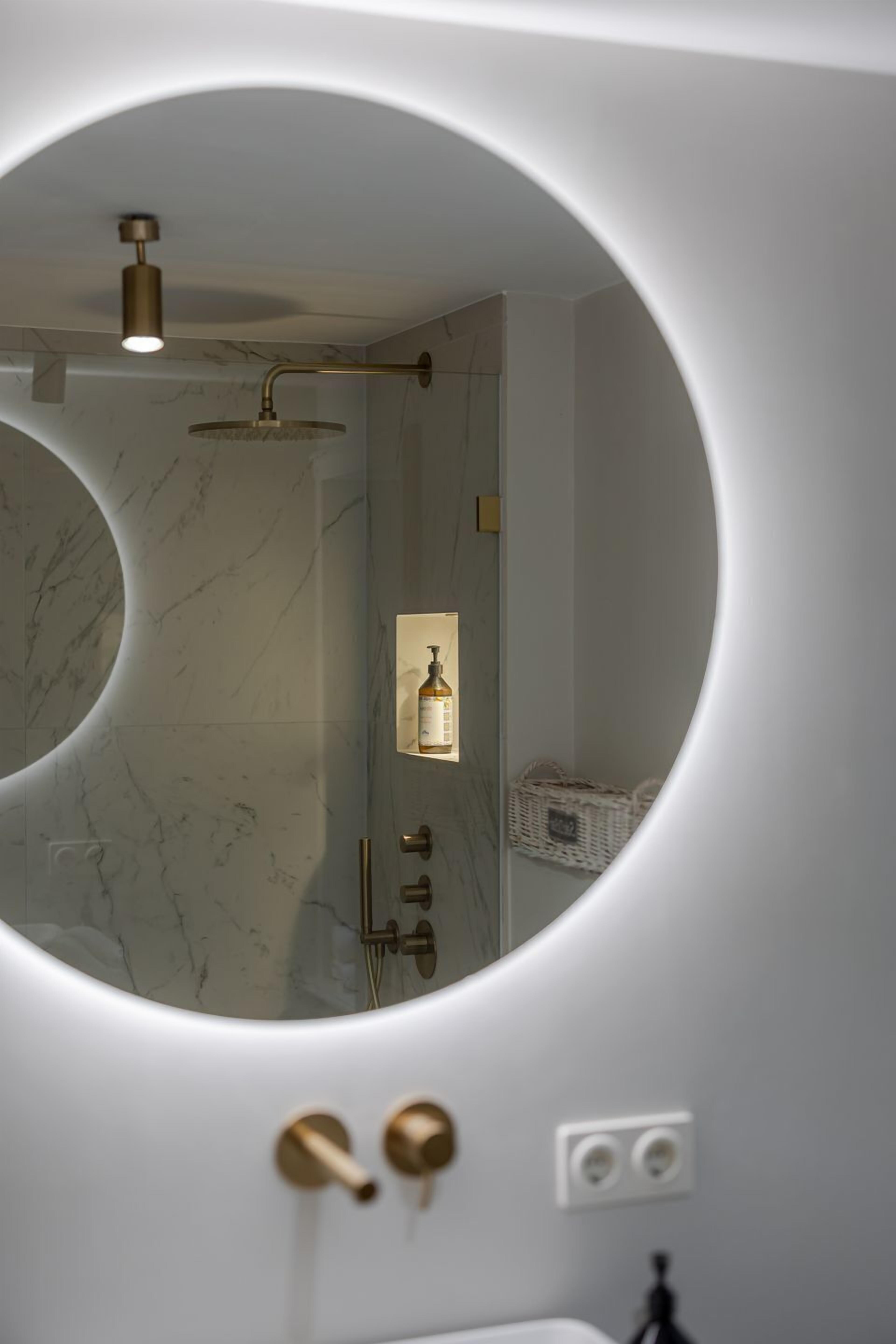 A bathroom with a circular mirror, a shower, and a bottle of shampoo on a shelf.