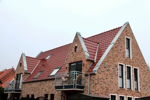 A multi-story brick building with a red-tiled roof, multiple windows, and a balcony with a metal railing. - Deichkrone - New Deichkrone vacation apartment with harbor view, balcony & (Krummhörn)