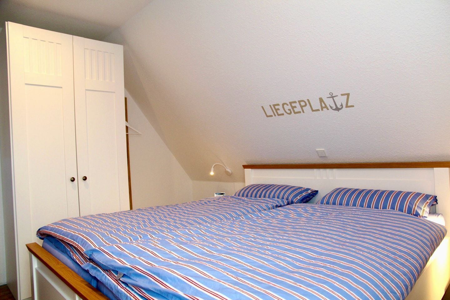 A bedroom with a bed, a wardrobe, and a wall with the text 'LIEGEPLATZ'.