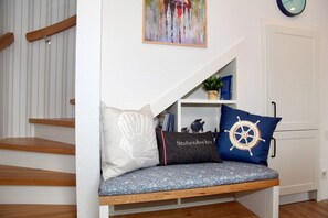 A bench with three cushions, a wall-mounted clock, and a bookshelf with books and a plant. - Deichkrone - New Deichkrone vacation apartment with harbor view, balcony & (Krummhörn)