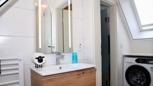 A modern bathroom with a wooden vanity, a sink, a mirror, a towel rack, a washing machine, and a skylight. - Deichkrone - New Deichkrone vacation apartment with harbor view, balcony & (Krummhörn)
