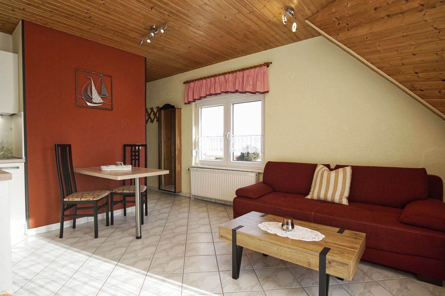 Een gezellige woonkamer met een rode bank, een houten salontafel en een eethoek met een tafel en stoelen.