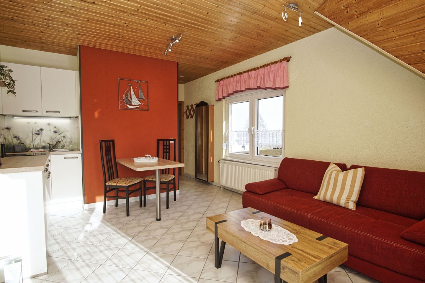 Un salon chaleureux avec un canapé rouge, une table basse en bois et un coin repas comprenant une table et des chaises.