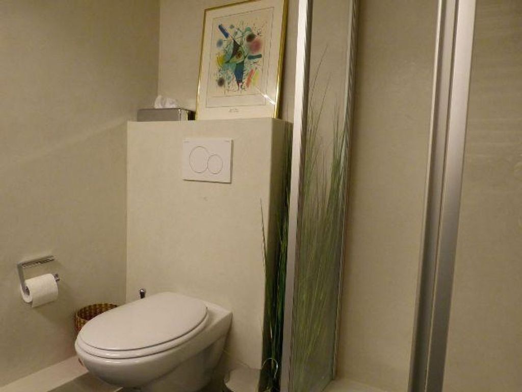 A bathroom with a toilet, a roll of toilet paper, and a framed picture on the wall.