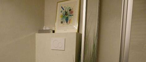 A bathroom with a toilet, a roll of toilet paper, and a framed picture on the wall.