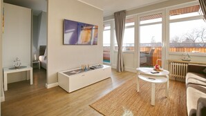 Een moderne woonkamer met een bank, een salontafel, een bijzettafeltje met decoratie, een schilderij aan de muur en een groot raam met gordijnen.