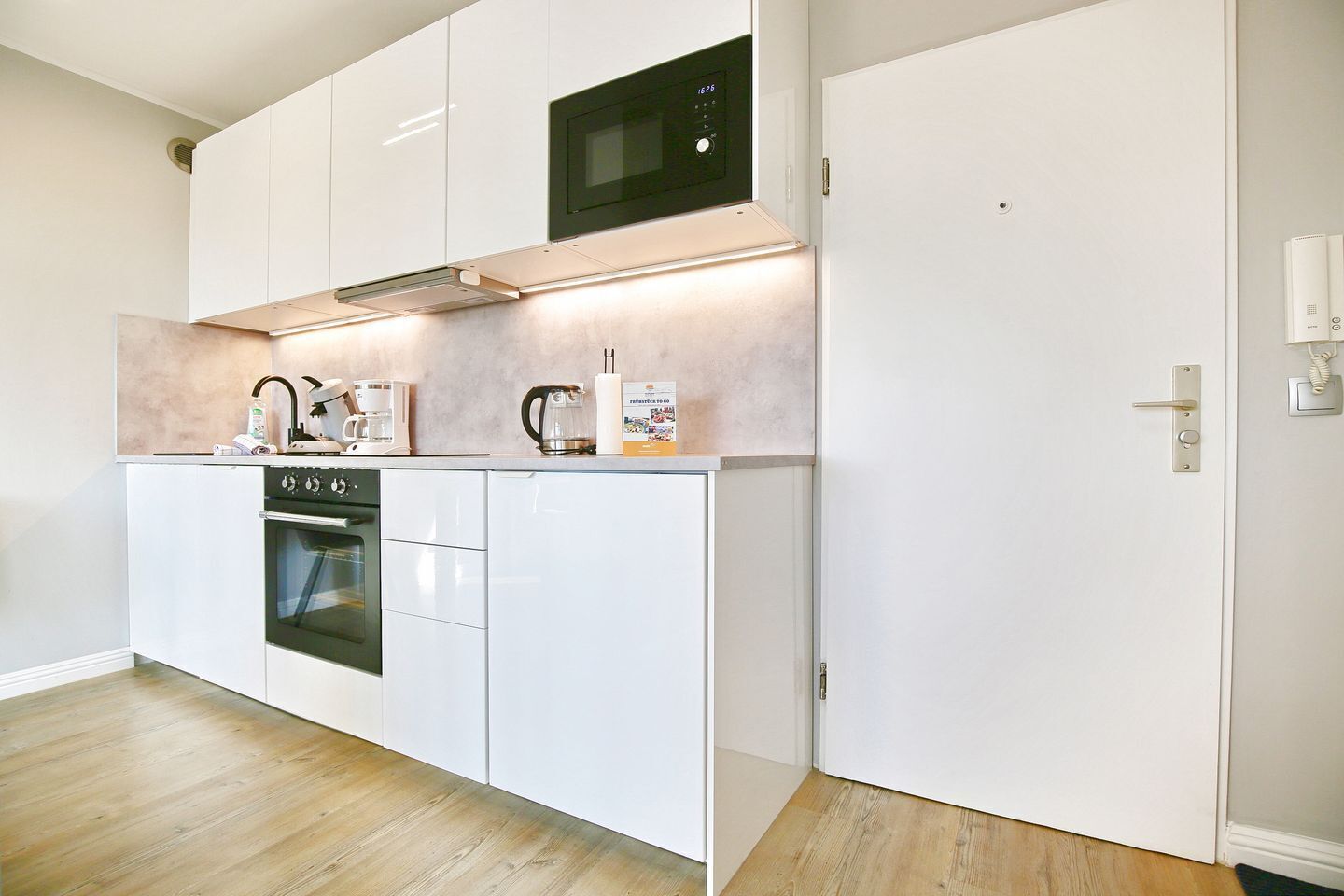 A modern kitchen with white cabinetry, a built-in oven, a microwave, and a coffee maker.