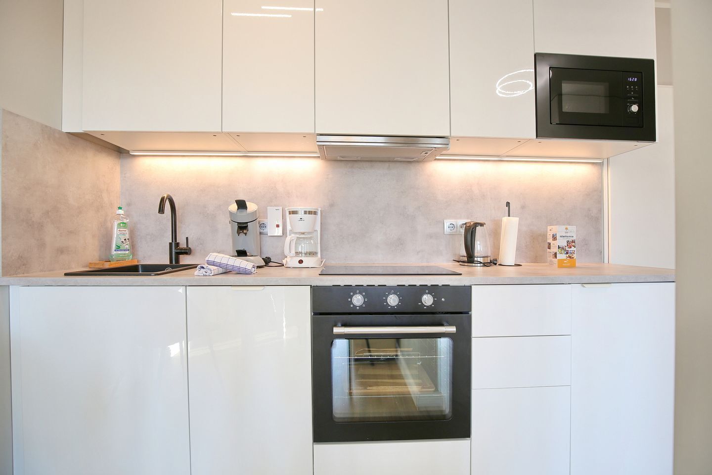 Une cuisine moderne avec des meubles blancs, un four encastré, une machine à café et un four à micro-ondes.