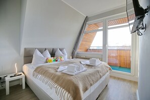 Un dormitorio con cama, almohadas, una mesita de noche, televisor y ventana con vista a una cerca de madera.