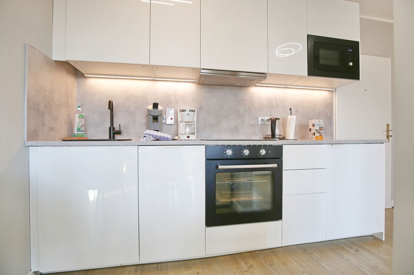 A modern kitchen with white cabinets, a built-in oven, a coffee maker, and a microwave.