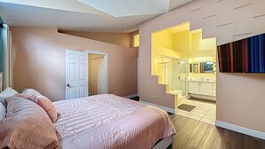 Une chambre à coucher avec un lit, une porte donnant accès à une salle de bain et un téléviseur fixé au mur.