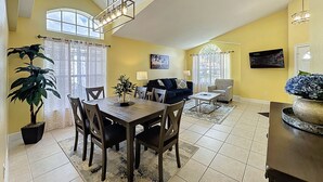 Un vaste espace de vie comprenant une table à manger, des chaises, un canapé et un téléviseur fixé au mur.