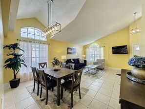 A spacious living area with a dining table, chairs, a sofa, and a TV mounted on the wall. - Beautiful 4 Bed Vacation Pool Home Near Disney/Universal (Kissimmee)