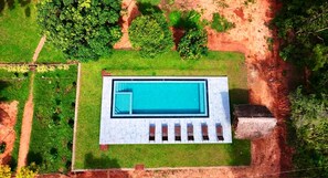 An aerial view of a rectangular swimming pool with a white deck, surrounded by green grass and trees. - Sigiriya nature Resort (Sigiriya,)