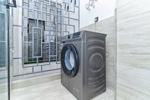 Eine kompakte, moderne Waschmaschine in einem Badezimmer mit Fliesenboden und einer Metalltür.